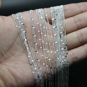 Assorted silver DIY chain necklaces including cross and wave styles held by hand