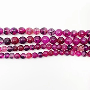 Detailed view of four rows of polished magenta dragon vein agate beads on white background