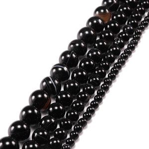 Detalle macro de cuentas de ágata negra natural con rayas en varios tamaños sobre blanco