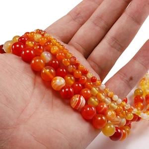 Primer plano de cuentas de ágata natural a rayas rojas y naranjas en la mano