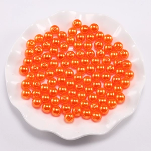 Vibrant orange ABS faux pearls for DIY jewelry making in a white decorative bowl