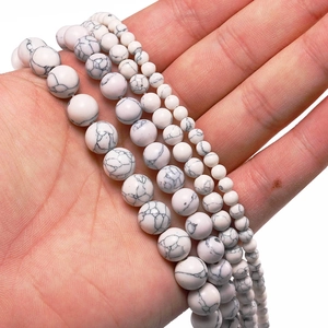 Detailed view of white howlite beads in four sizes held in hand for jewelry making