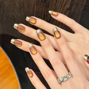 Braune Katzenauge-Kunstnägel mit goldenen French-Spitzen und weißen Konturen