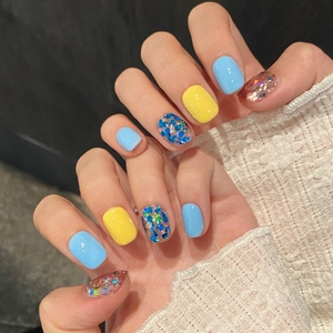Short round press-on nails in light blue and yellow with colorful sequins and knit cuff