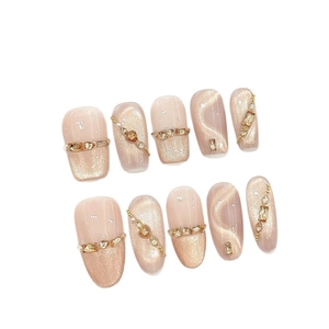 Faux ongles œil-de-chat champagne avec chaînes de cristaux 3D et perles sur fond blanc
