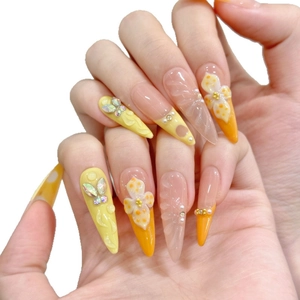 Vibrant orange and yellow stiletto nails with 3D floral accents and crystal butterflies