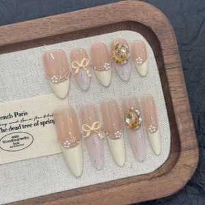 Faux ongles French avec nœuds crème, strass champagne et paillettes argentées