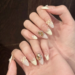 Faux ongles amande crème avec nœuds 3D, perles, strass ambre et paillettes argentées