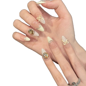 Faux ongles crème avec nœuds 3D, strass et perles sur une forme d'amande longue élégante