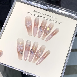 Detail of nude pink nails with 3D floral accents, pearls, and glitter on beige paper