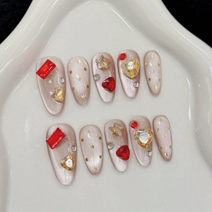 Cat eye press-on nails with red rhinestones and golden heart accents on almond shape
