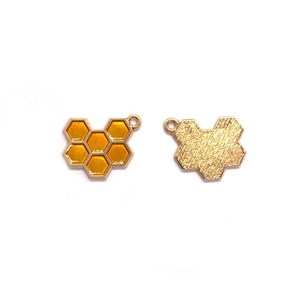 Detalle de dijes en forma de panal con esmalte naranja y reverso de metal dorado texturizado