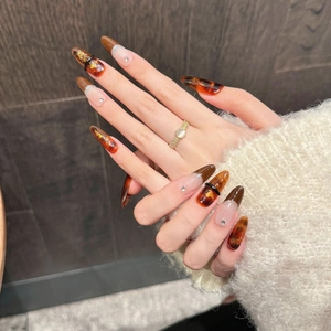 Brown amber almond press-on nails with gold foil and French rhinestones on wood background