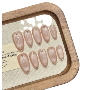 Nude almond press-on nails with white polka dots and crystals on wood tray