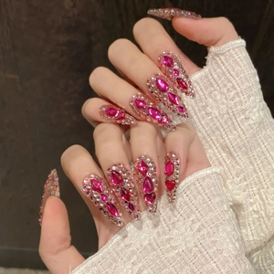 Stiletto press-on nails with luxury pink rhinestones and heart crystals on dark background