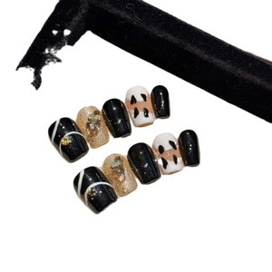 Handmade press-on nails set featuring black, white, and gold designs with rhinestones