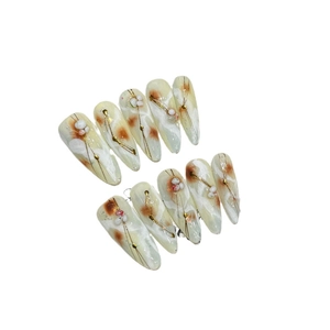 Handcrafted marble press-on nails with amber tones and gold wire accents in long stiletto shape