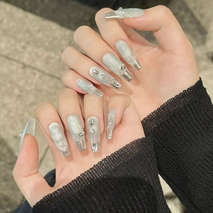 Detail of handmade cat-eye press-on nails with silver glitter, white bamboo leaves and pearls