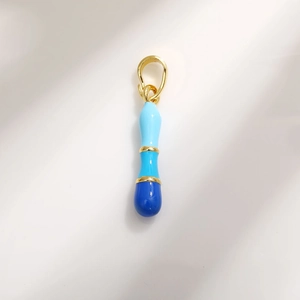 Close-up of a gradient blue enamel capsule charm with gold plating and hook detail