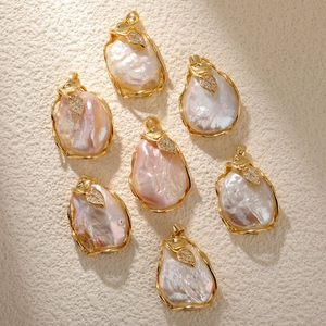 Baroque pearl leaf pendants with gold plating and zircons on a textured stone base