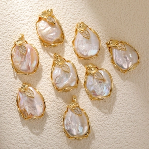Baroque freshwater pearl pendants with gold leaf accents and tiny crystals on a beige surface