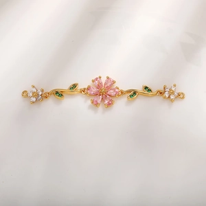 Elemento per bracciale a fiore dorato con petali rosa e foglie verdi su sfondo chiaro