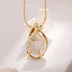 Macro view of gold ginkgo leaf pendant with baroque pearl and shimmering zircon on bead chain