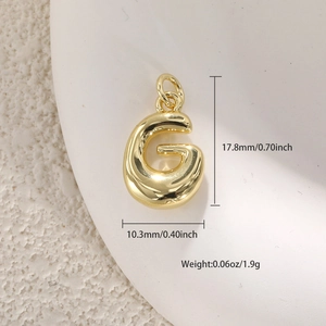 Vista macro de un colgante de letra G inflado bañado en oro de 18k con medidas en pulgadas