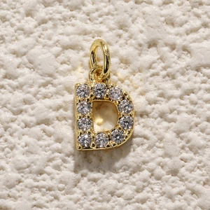 Macro-opname van vergulde hanger letter D met micro-pave zirkoon op stenen achtergrond