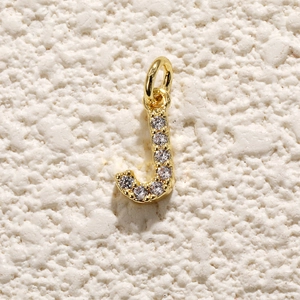 Macro-opname van een vergulde letter J hanger met zirkonia inlays en een klein ringetje