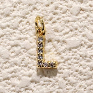 Detailopname van gouden letter L hanger met zirkonia steentjes op getextureerde achtergrond