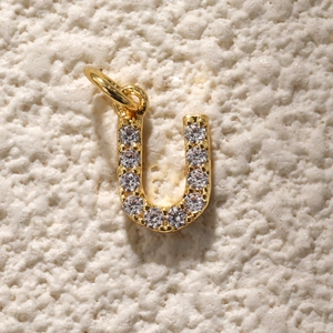 U-vormige gouden hanger met zirkonia inleg op een witte stenen ondergrond