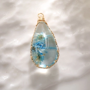 Teardrop pendant with blue dried flower in resin and golden wire wrap detail