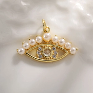 Golden evil eye pendant with pearls and zircon crystals on a warm textured surface
