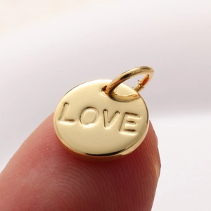 Macro shot of a small gold 'LOVE' engraved round charm held on a fingertip for DIY jewelry