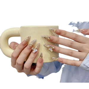 Pink stiletto press-on nails with 3D butterflies and glitter on a cream mug backdrop