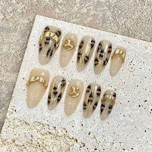Detailed view of handmade almond nails with gold embossing and amber leopard patterns