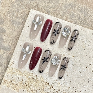 Handmade cherry red press-on nails with rhinestone accents and floral nail art
