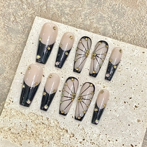 Handmade press-on nails with nude French tips, black spiderweb patterns, and gold rhinestones