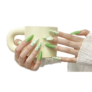 Long almond press-on nails in lime green with luxury crystal rhinestones holding a cup