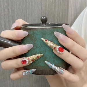Close-up of stiletto press-on nails with vintage gold relief, gems, and pearls on hands