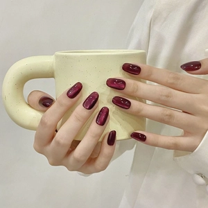 Ongles press-on œil de chat violet foncé présentés sur une main tenant une tasse