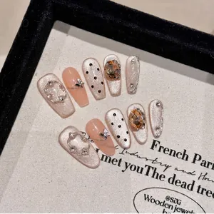 Champagne pink handmade press-on nails with amber gems and butterfly charms on canvas