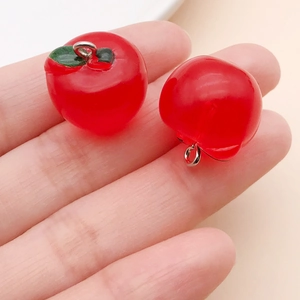 Detailed view of two red resin apple pendants with green leaf and silver metal rings