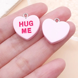 Détail de pendentifs cœur en résine rose avec texte HUG ME rouge pour bijoux DIY