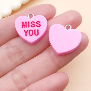 Close-up of a pink resin heart charm with red MISS YOU text and small metal ring
