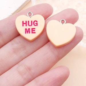 Gros plan de pendentifs en résine en forme de cœur avec texte Hug Me et anneaux