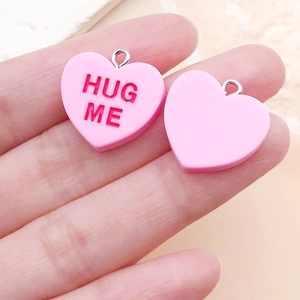 Gros plan de pendentifs cœur en résine rose avec texte HUG ME et boucles en métal argenté