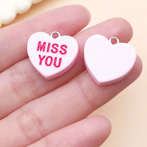 Detail of pink resin heart charm featuring red MISS YOU text and silver metal loop