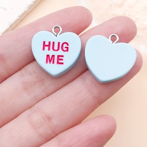 Détail du pendentif cœur en résine bleu clair avec texte Hug Me tenu dans la main